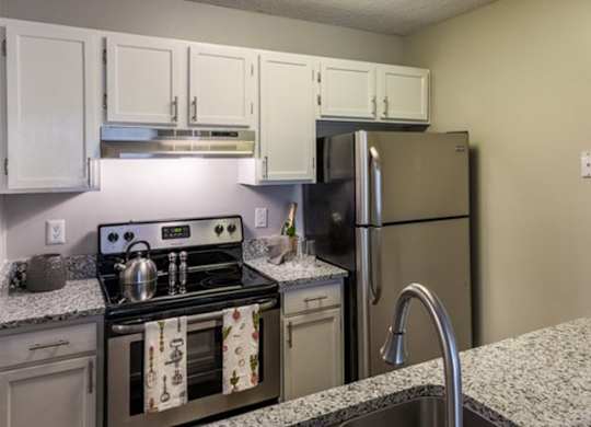 A kitchen with a stove, oven, refrigerator, and cabinets.