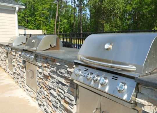 A row of outdoor grills are lined up on a stone wall.
