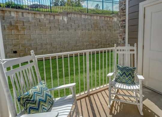 Two white chairs with green pillows sit on a wooden deck.