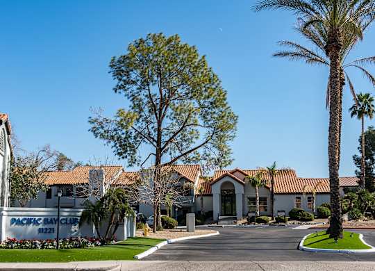 Ahwatukee, AZ, Apartments for Rent - Pacific Bay Club - Property Exterior with White Walls, Terracotta Roofing, Driveway, and Palm Trees.