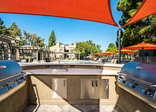 Two-Bedroom Apartments In Walnut Creek, CA - Park Lake At Walnut Creek - Outdoor Kitchen With BBQ Grills Under A Canopy In Front Of The Pool With Umbrellas And Lounge Chairs