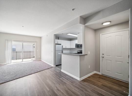 an empty living room and kitchen with a door to a balcony