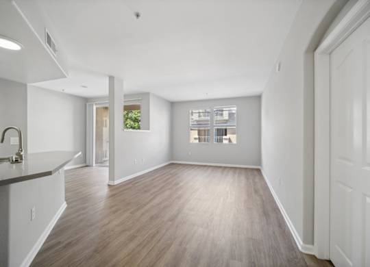 an empty living room and kitchen with white walls and wood floors