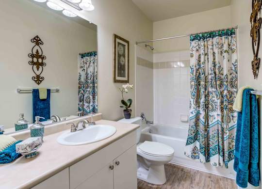 A bathroom with a white toilet, a sink, a mirror, a shower curtain, and a towel rack.
