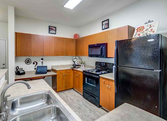 A kitchen with a black refrigerator, wooden cabinets, and a stainless steel sink.