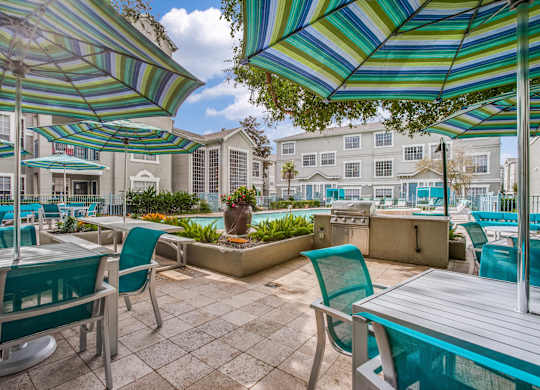 Luxury 2-Bedroom Apartments in Houston, TX - The Maroneal - BBQ/Picnic Area with Tables, Chairs, Umbrellas, a Grilling Station, and a View of the Pool