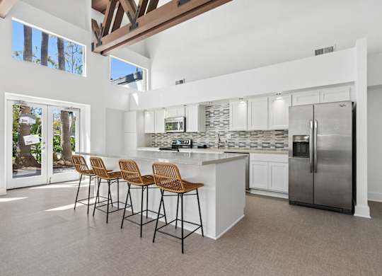A kitchen with white cabinets and a large island with a refrigerator on the side.