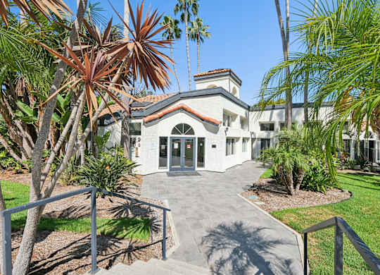 A white building with a red roof is surrounded by palm trees.
