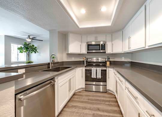 San Clemente, CA Apartments - Rancho Del Mar - Kitchen with White Cabinets, Grey Countertops, Deep Basin Sink, and Stainless Steel Appliances.