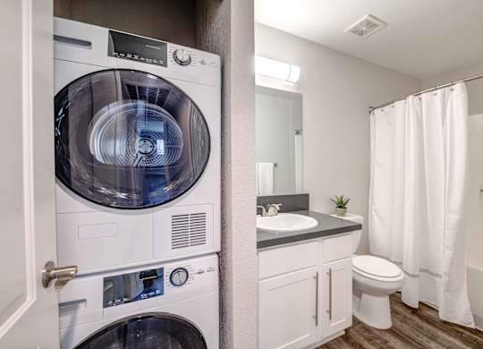 Apartments in San Clemente, CA - Rancho Del Mar - Bathroom with Hardwood-Inspired Flooring, a Toilet, a Shower, a Vanity with White Cabinets, and an In-Unit Washer/Dryer