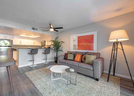 San Clemente, CA Apartments for Rent - Rancho Del Mar - Living Room with Couch, Area Rug, Floor Lamp, Ceiling Fan, Coffee Table, and Access to Kitchen.