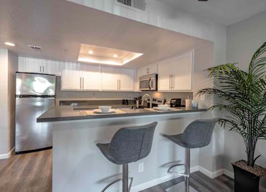 One-Bedroom Apartments in San Clemente, CA - Rancho Del Mar - Modern Kitchen with White Cabinets, Stainless Steel Appliances, Grey Countertops, High Top Seating, and Stylish Decor