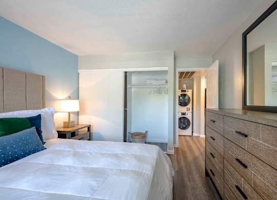 Two Apartments in San Clemente, CA - Rancho Del Mar - Bedroom with Wood-Style Flooring, Nightstand with Lamp, Dresser, Mirror, Spacious Closet with Sliding Door, and View of Washer and Dryer.