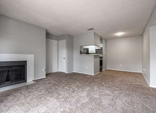 A spacious living room with a fireplace and a kitchenette in the background.