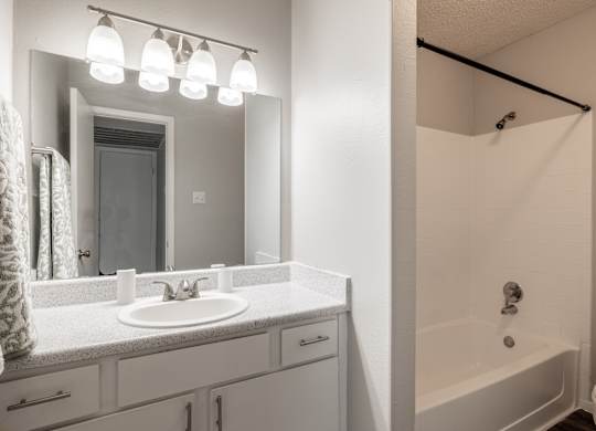 A white bathroom with a sink, mirror, and bathtub.