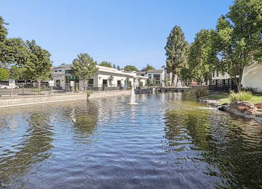 A serene pond with a fountain in the middle surrounded by trees and buildings.
