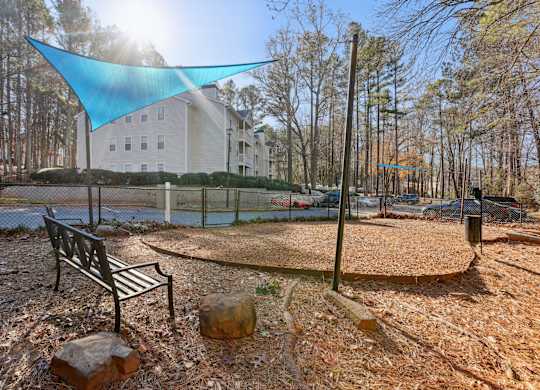 A park with a bench and a blue shade sail.