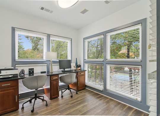 A home office with a desk, chairs, and a computer setup.