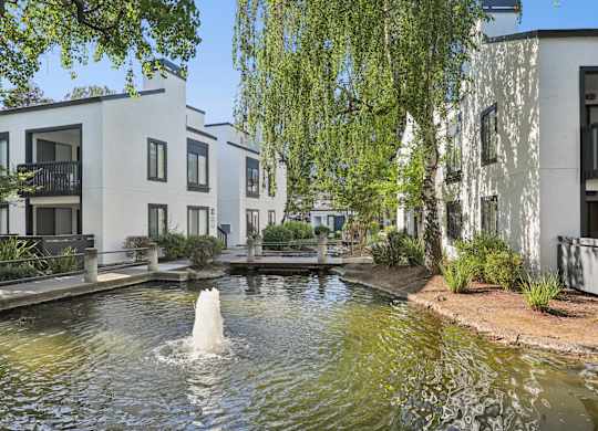 A fountain in the middle of a pond in front of apartment buildings.