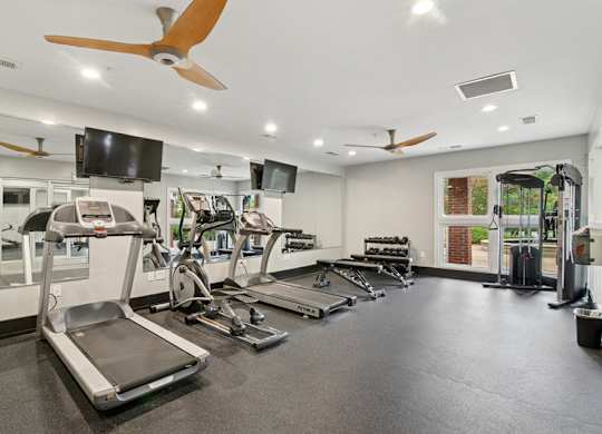 A gym with treadmills, elliptical machines, and a television.