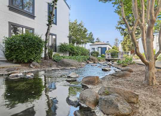 A stream flows through a landscaped garden in front of a white house.