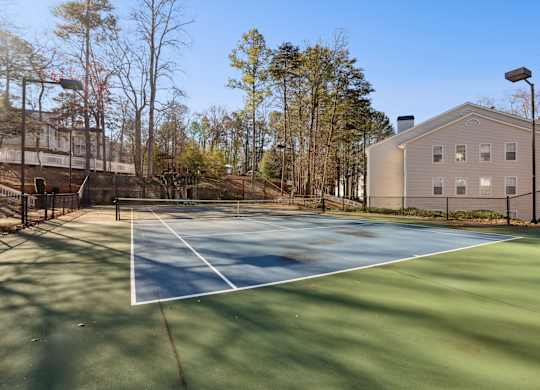 A tennis court is surrounded by a fence and a building.