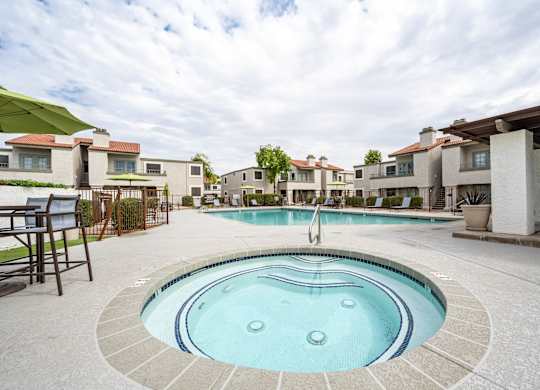 Apartments Scottsdale, AZ - The Sycamore at Scottsdale - An exterior view the pool with gated entry featuring lounge seating, umbrellas, and nice landscaping