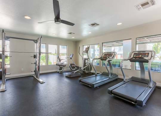 A spacious gym with treadmills, elliptical machines, and a fan.