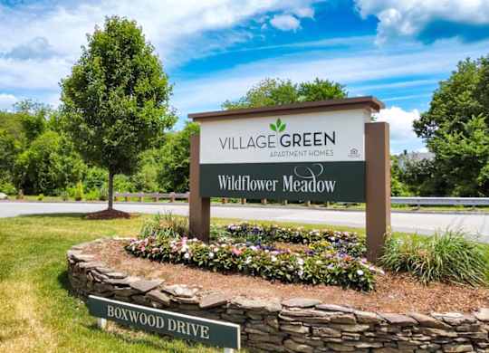 a stone retaining wall with flowers in front of a sign that says village green wildflower me