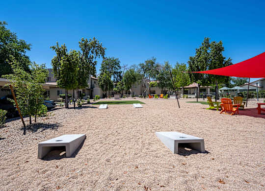Two-Bedroom Apartments in Ahwatukee, Phoenix, AZ - Village at Lakewood - Outdoor Area with Cornhole Boards, Tall Trees, and a Red Canopy.