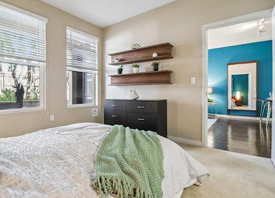 A bedroom with a bed covered in a white blanket and a green throw.