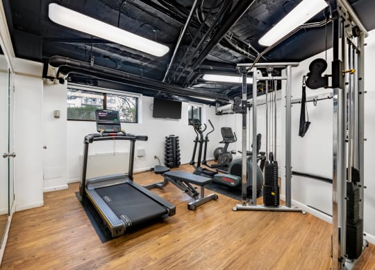 a gym with exercise equipment and weights in a room with white walls and wood floors
