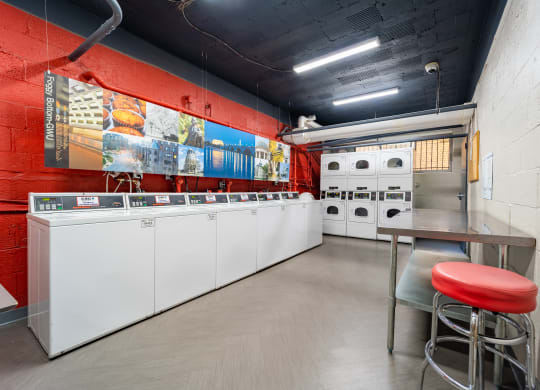 a laundry room with washing machines and a table with a red stool