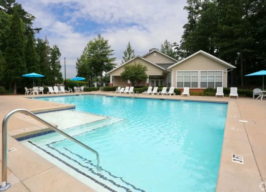 a swimming pool with chairs and a house in the background