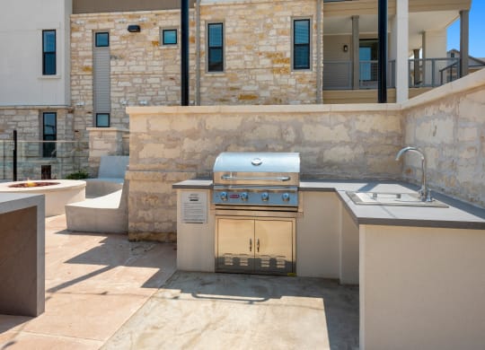 an outdoor kitchen with a grill and a sink in a backyard