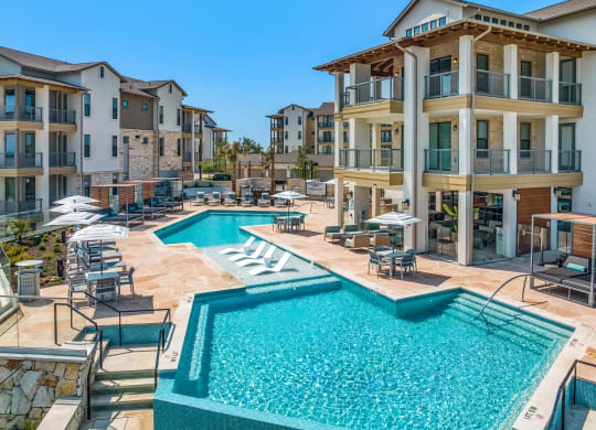 a swimming pool with chairs and umbrellas in front of an apartment building
