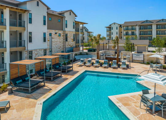 a swimming pool with chairs and umbrellas in front of an apartment building
