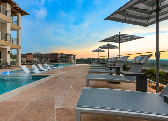 a pool with lounge chairs and umbrellas next to a building