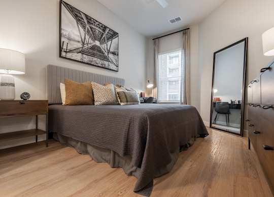 A bedroom with a bed, nightstand, and a painting on the wall.