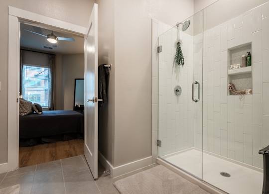 A bathroom with a walk-in shower and a bedroom with a window.