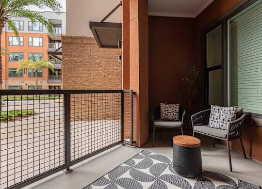 A patio with a black metal fence, a grey sofa, and a black and white patterned rug.