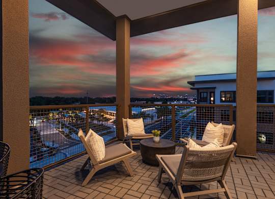 A balcony with chairs and a table overlooking a body of water at dusk.