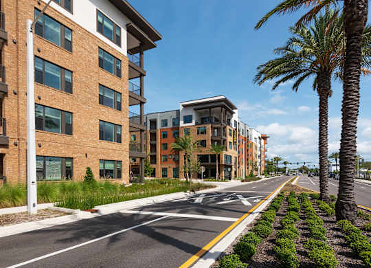 A street view of a residential area with modern buildings and palm trees.