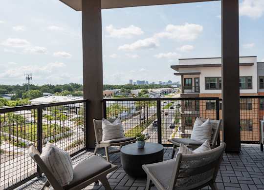 A balcony with a table and chairs overlooking a cityscape.