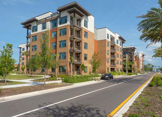 A multi-story apartment building with a sign that says "Now Leasing" is shown.