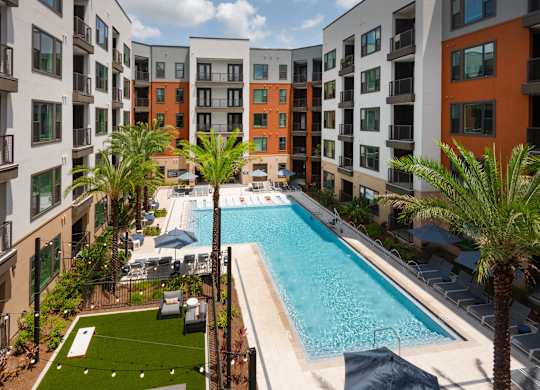 A swimming pool surrounded by palm trees and lounge chairs in a courtyard.