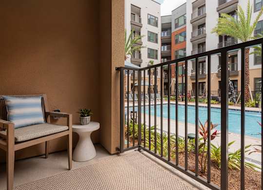 A chair with a blue pillow is on a patio next to a pool.