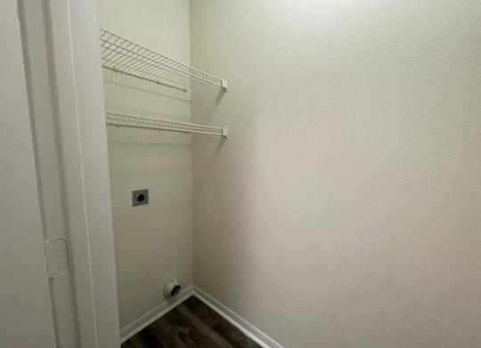 A white closet with a door open and a light switch on the wall.
