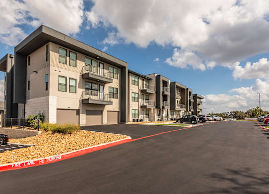 A street view of a residential area with apartment buildings on the left and cars parked on the right.