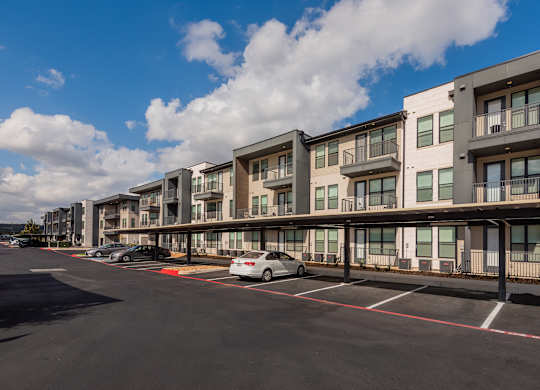 A row of modern apartment buildings with cars parked in front.